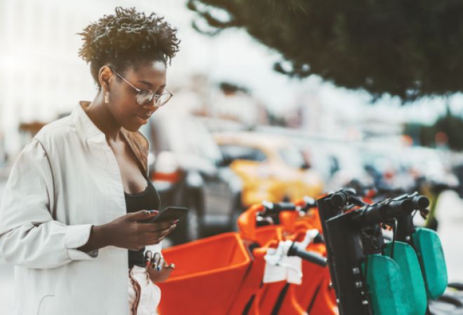 Young woman using her phone to hire an e-scooter